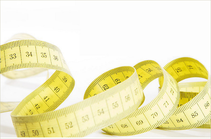 A yellow measuring tape coiled in various loops showing markings for inches and centimeters.