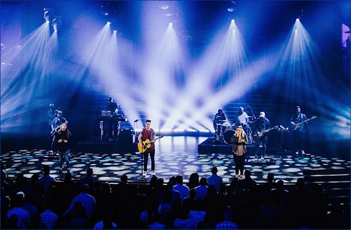 A live music performance on stage with several musicians playing instruments, illuminated by dramatic lighting effects.