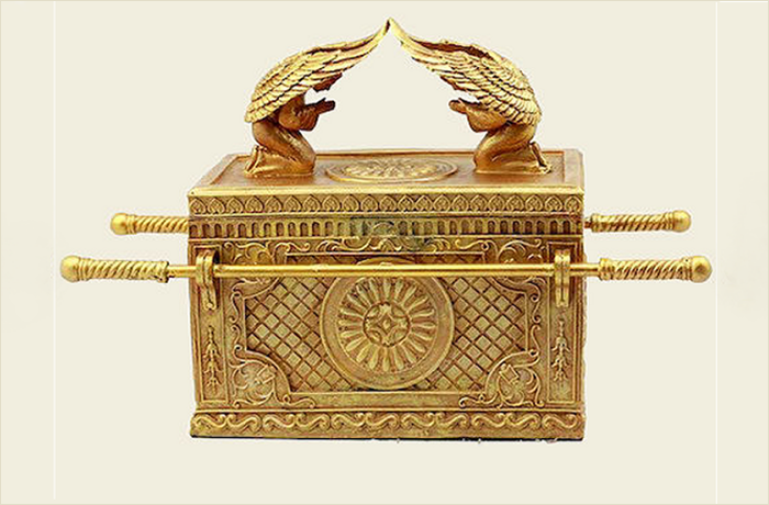 A golden ornate box with winged figures on top, intricate carvings, and two handles on the sides.