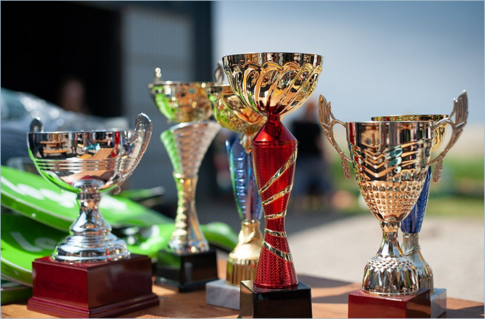 A collection of shiny trophies in various designs and colors, including silver and red, placed on a table outdoors.