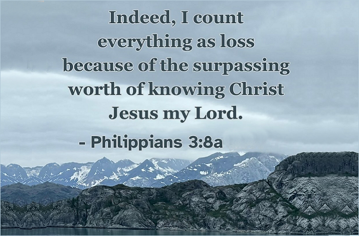 A scenic landscape featuring mountains and a cloudy sky, with a biblical quote from Philippians 3:8 overlaid in bold text.